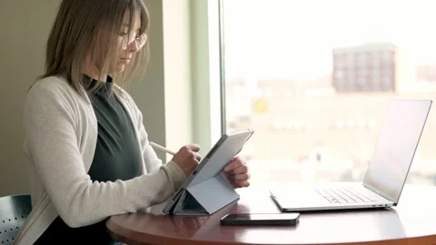 A professional designer efficiently multitasks using a tablet and laptop in a Stock Footage 274656761