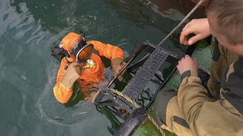 Professional diver stands in cold water, holding ships ladder, get ready to dive Stock Footage 101013533