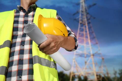 Professional electrician with drafting and helmet near high voltage tower, cl Stock Photos