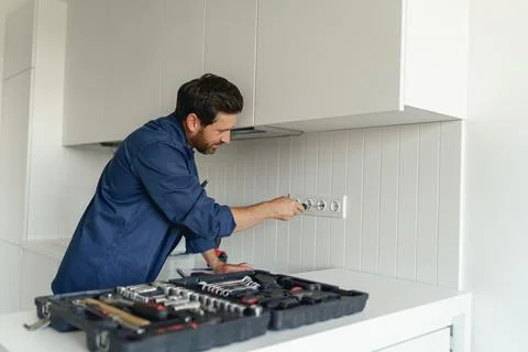 Professional electrician using screwdriver while installing new electrical Stock Photos