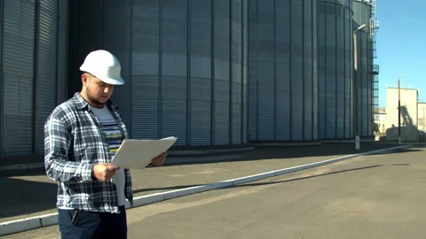 Professional engineer with blueprints inspecting agricultural silos Stock Footage 142604319