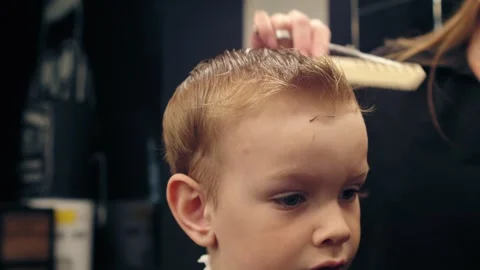 Professional female barber cutting a young boy's hair in a modern barbershop Stock Footage 335504853