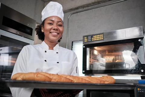 Professional female chef with baking bread, cheerful smile in the kitchen. Stock Photos