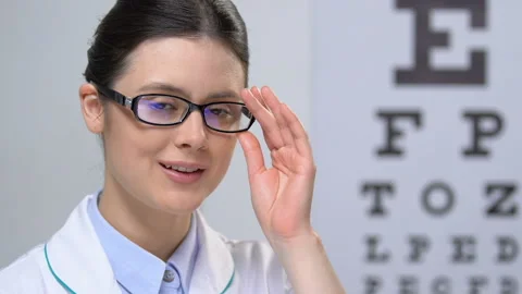 Professional female optician looking at camera against eye chart background Stock Footage 110692570