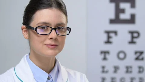 Professional female optician looking at camera against eye chart background Stock Footage 110697784