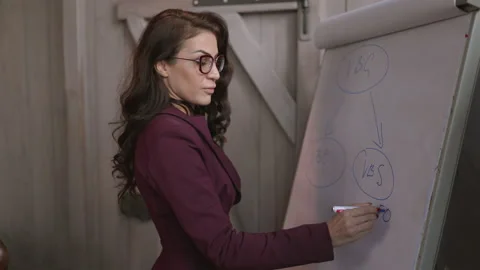 A professional female presenter is engagingly explaining concepts on a flip Stock Footage 312177833