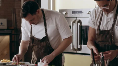 Professional focused chef carefully placing ingredients onto a plate with help f Stock Footage 199458653