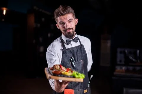Professional friendly flunky helpfully holds plate with prepared dish at a Foto stock