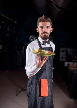 Professional friendly flunky helpfully serves appetizing dish on a black Foto stock