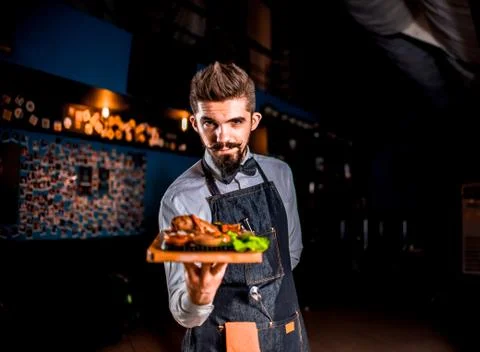Professional friendly waiter serves appetizing dish on a black background. Foto stock