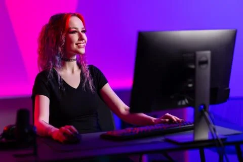 Professional gamer smiling while playing a PC game in a vibrant room with neon Stock Photos