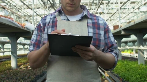 Professional gardener in apron writing notes on clipboard working in greenhouse Stock-Footage 118913717
