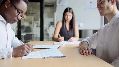 Professional hands sign documents at a table. Two men shake hands, completing a 스톡 동영상 335733458