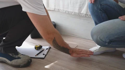 Professional handyman inspecting damaged laminate flooring with female cust.. Stock Footage 345152938