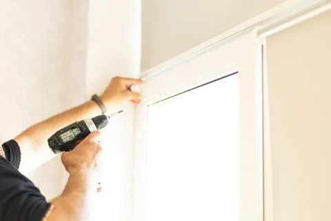 Professional handyman installing modern roller blinds on home windows. Stock Photos