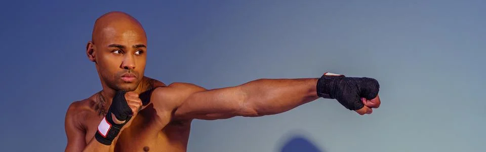 Professional kickboxer is training and practicing punch on studio background Stock Photos
