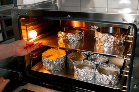In a professional kitchen a baker inserts a baking tray with cake molds into the Stock Photos