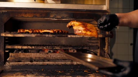 A professional kitchen chef in a black jacket near a hot grill oven takes ribs Stock Footage 276303331