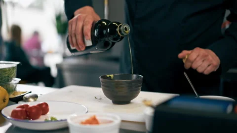 In a professional kitchen a chef in a black jacket pours olive oil for toast Stock Footage 276870869