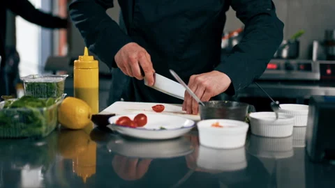 In a professional kitchen chef in a black jacket cuts tomato for toast with Stock Footage 276871356