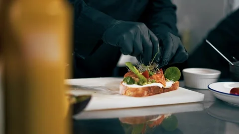In a professional kitchen chef in a black jacket decorates a prepared toast with Stock Footage 276873880
