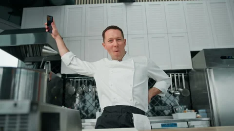 Professional kitchen chef in uniform with phone in hand is emotionally happy to Stock Footage 237976682