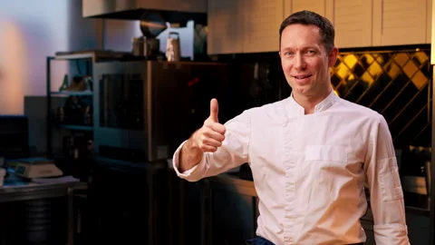 Professional kitchen smiling and satisfied chef in white coat stands with his Stock Footage 273563079