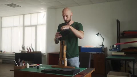 Professional leather craftsman rises from the work table to use retaining clip Stock Footage 254726934