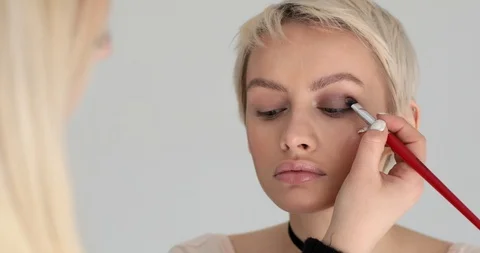 Professional make up artist applying eye shadows on female face indoors  Stock Footage 90929366