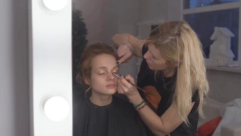 The professional make-up artist does make-up for the young cute model. two Stock Footage 83785420