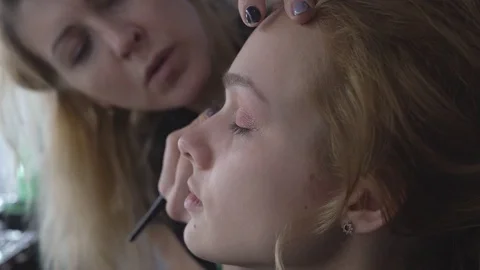 The professional make-up artist does make-up for the young cute model. two Stock Footage 83785649