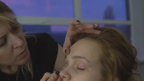 The professional make-up artist does make-up for the young cute model. two Stock Footage 83785727