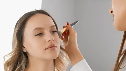 Professional makeup artist applying blush to a young womans face in a modern Stock Footage 341035458