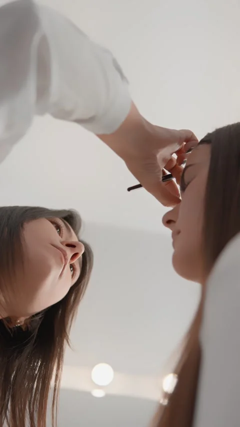 Professional makeup artist applying eyebrow makeup to a young woman in a modern Stock Footage 340922695