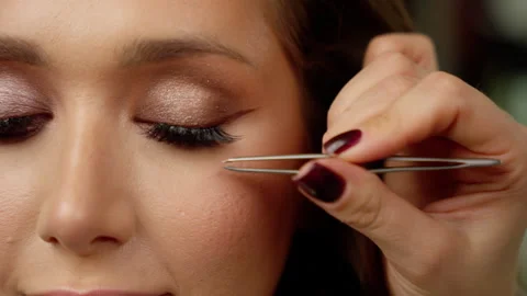 Professional makeup artist applying false eyelashes with precision tweezers Stock Footage 304358091
