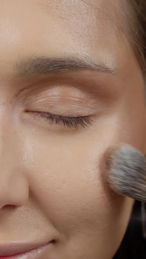Professional makeup artist blending foundation on models cheek, showcasing Stock Footage 304334608
