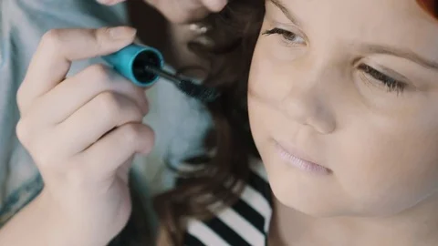 Professional makeup. Make-up artist paints eyelashes to a little sweet girl, use Stock Footage 77825571