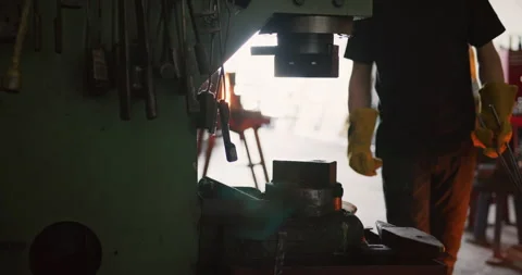 Professional male blacksmith walking to a machine to press a piece of red hot ir Stock Footage 199460866