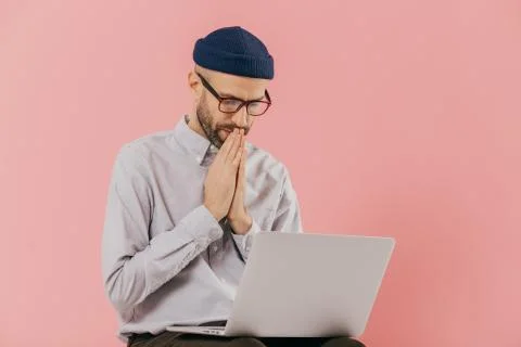 Professional male programmer keeps hans in praying gesture, looks at screen o Stock-Fotos
