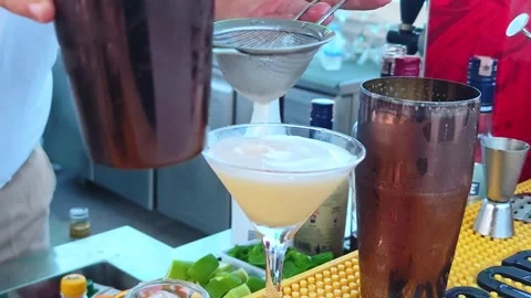 Professional man bartender pouring cocktail drink in cocktail glass from shaker. Vidéo 336996077