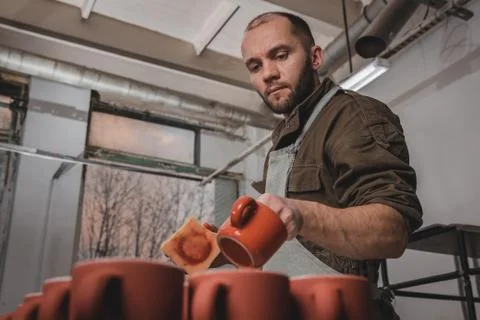 Professional man potter or decorator painting ceramic clay cup in red color i 写真素材