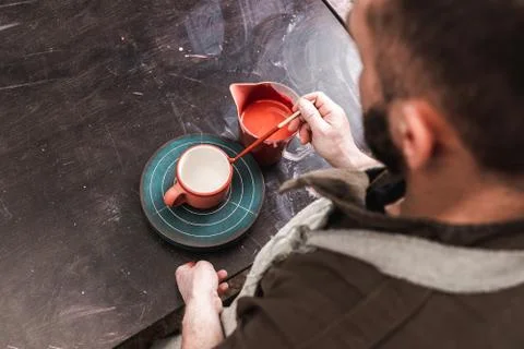 Professional man potter or decorator painting ceramic clay cup in red color i 스톡 사진