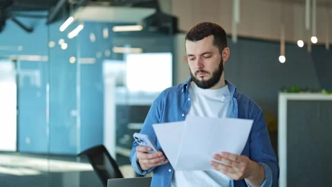 Professional Man Reviews Documents With Smartphone in Modern Office Stock-Footage 329091566
