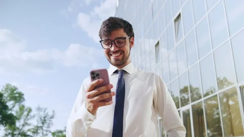 Professional man smiles while using smartphone outside modern office building Stock Footage 316050529