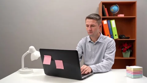 Professional man typing on a laptop computer and grabbing a sticky note that is Stock Footage 149743667