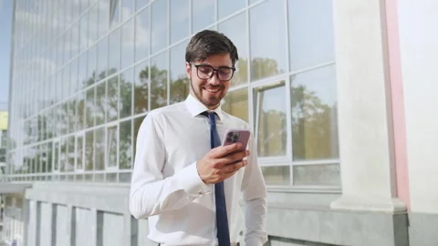 Professional man using smartphone outside a modern office building during bright Stock Footage 316050112