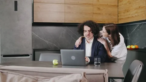 A professional man working on his laptop in a modern kitchen, while his wife Stock Footage 296832496