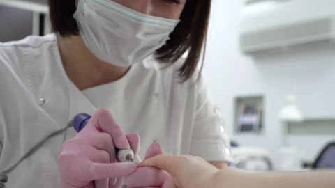 A professional manicurist using a drill tool cuts off old nails close-up. Nail Stock Footage 155972617