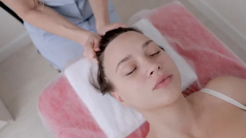 Professional masseur doing a head massage of a young beautiful girl in a spa Stock Footage 234993864