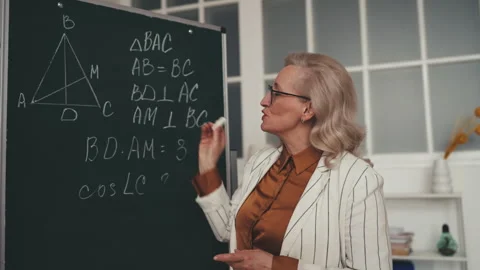 Professional math teacher in her 50s explaining geometry formula near blackboard Stock Footage 251859573